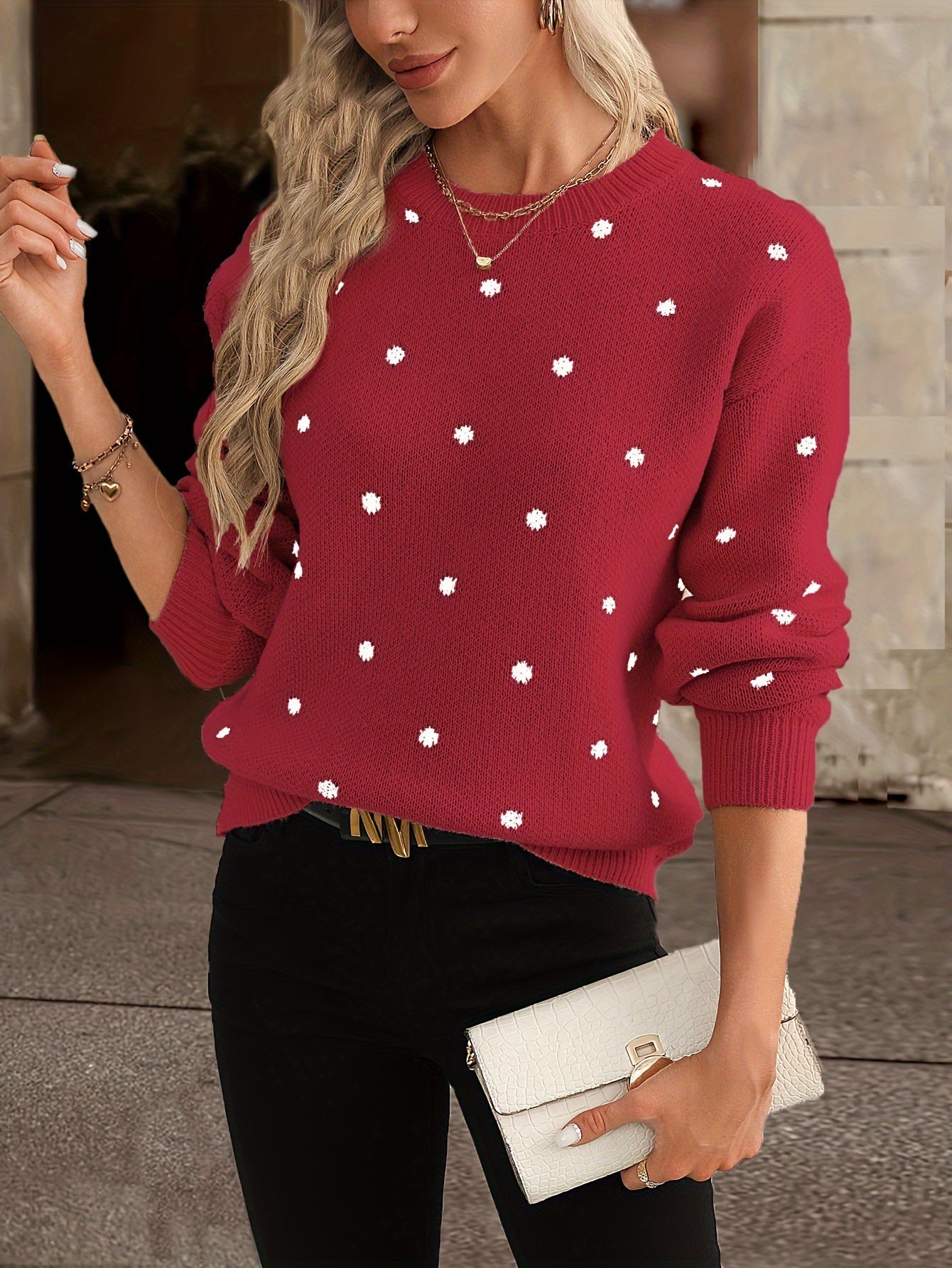 Femme portant un pull rouge à pois blancs, tenant une pochette blanche. Mode automne, style décontracté chic, tenue élégante pour femme.