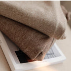 Deux couvertures en laine beige et marron à motif chevron, posées sur un livre, créant une ambiance cosy et chaleureuse.