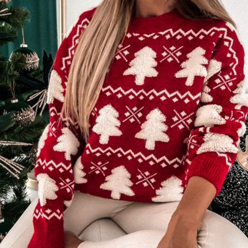 Femme portant un pull rouge de Noël avec motifs sapins blancs, assise près d'un sapin décoré. Mode hiver, vêtements festifs, style décontracté.