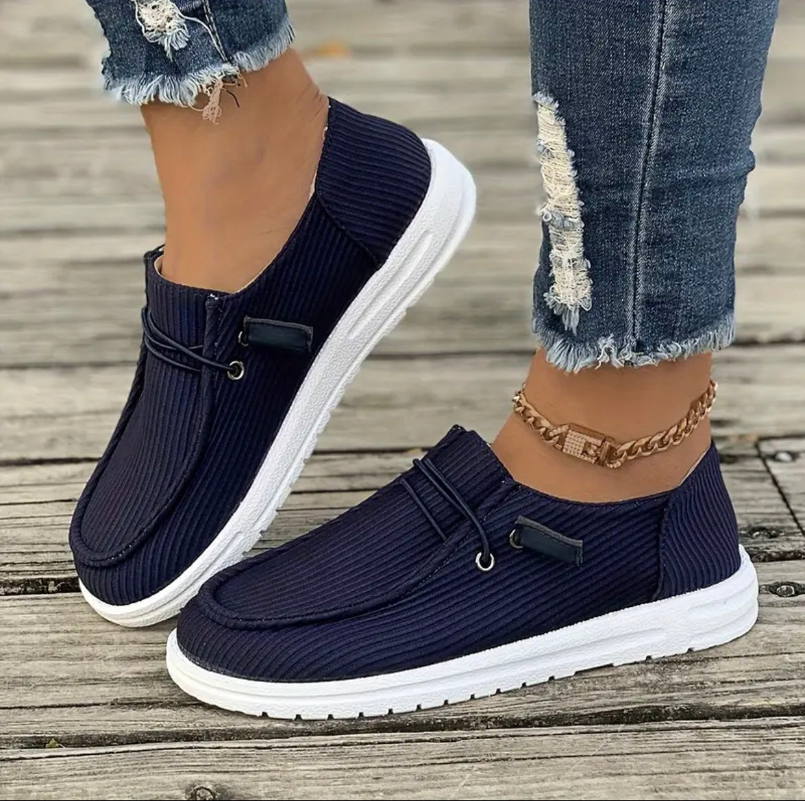 Chaussures décontractées bleu marine pour femme, semelle blanche, portées avec un jean déchiré. Style moderne et confortable pour la mode urbaine.