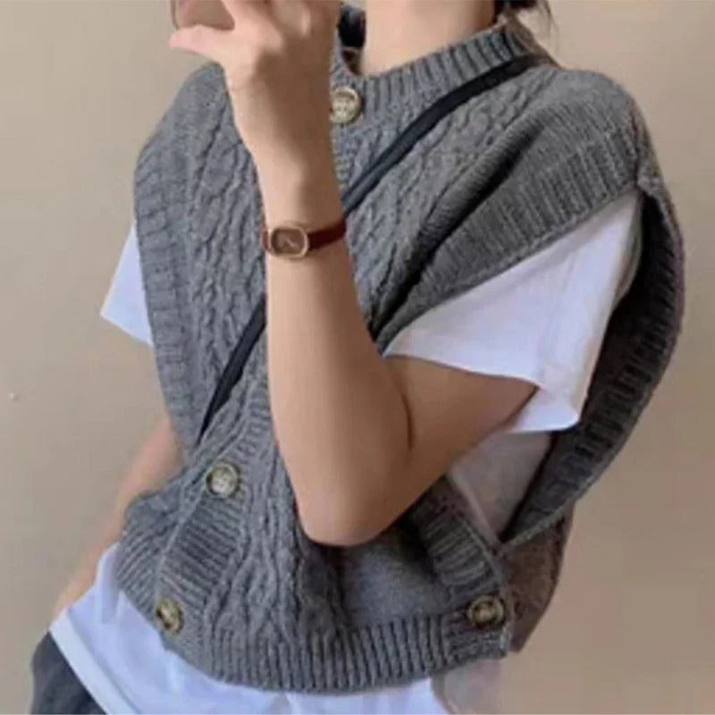 Femme portant un pull sans manches gris en tricot torsadé sur un t-shirt blanc, accessoirisé d'une montre-bracelet marron. Mode automne chic.