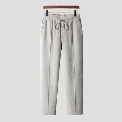 Pantalon gris en laine, coupe droite, avec cordon de serrage à la taille, poches latérales, suspendu sur un cintre en bois. Mode hiver élégante.
