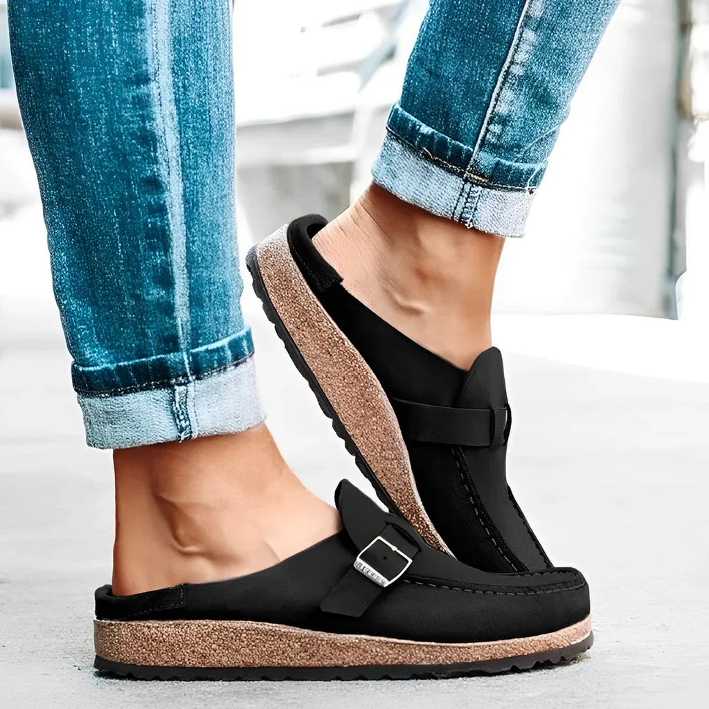 Chaussures mules noires en cuir avec semelle en liège, portées avec un jean bleu. Confortables et tendance, idéales pour un style décontracté.