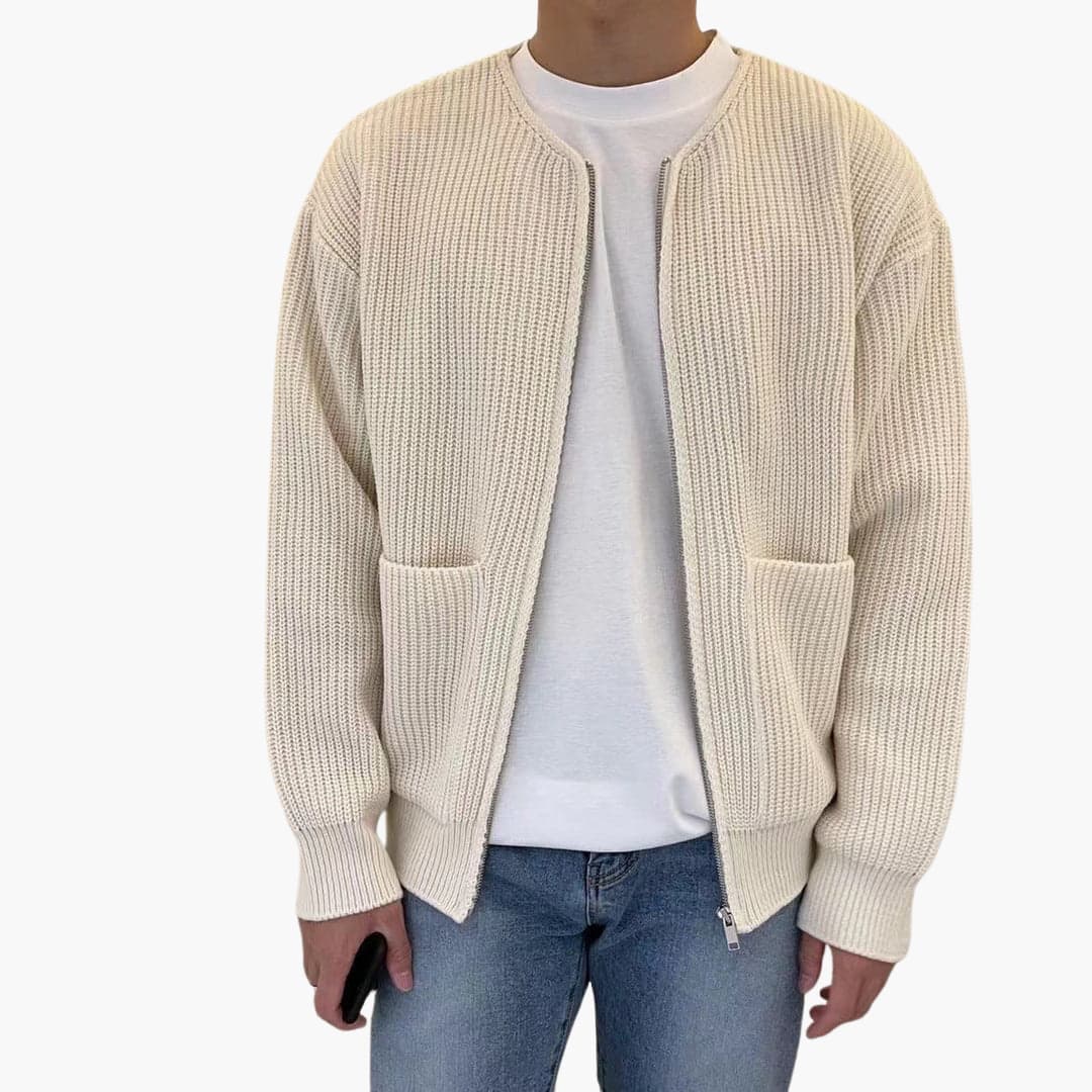 Homme portant un cardigan beige en maille avec poches, sur un t-shirt blanc et un jean bleu. Mode décontractée, style automne-hiver.