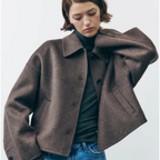 Jeune femme portant une veste marron en laine, col chemise, manches longues, sur un pull gris, avec un jean bleu. Mode automne-hiver élégante.