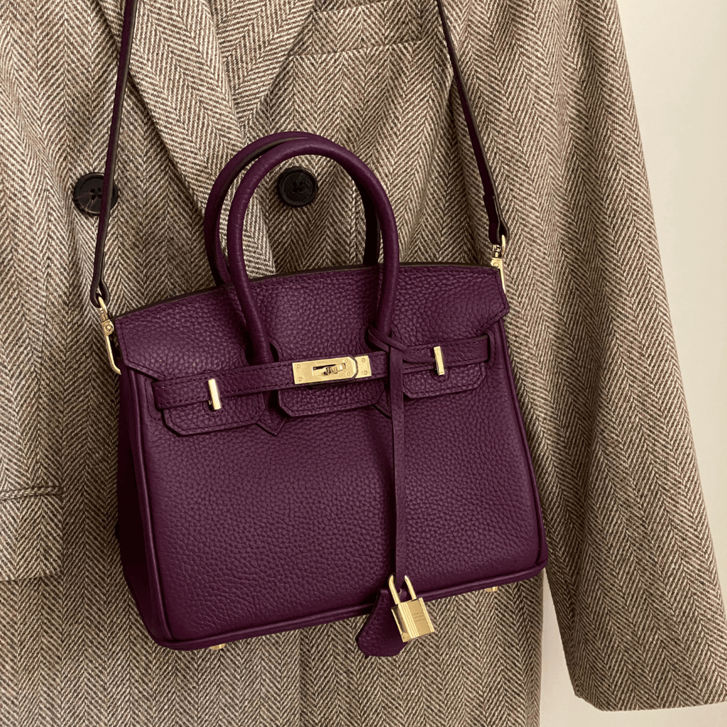 Sac à main en cuir violet avec fermoir doré, suspendu à un manteau en tweed marron. Accessoire de mode élégant et tendance.
