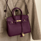 Sac à main en cuir violet avec fermoir doré, suspendu à un manteau en tweed marron. Accessoire de mode élégant et tendance.