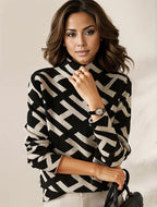 Femme élégante portant un pull à motifs géométriques noir et beige, montre-bracelet chic, tenant un sac à main noir. Mode automne-hiver tendance.