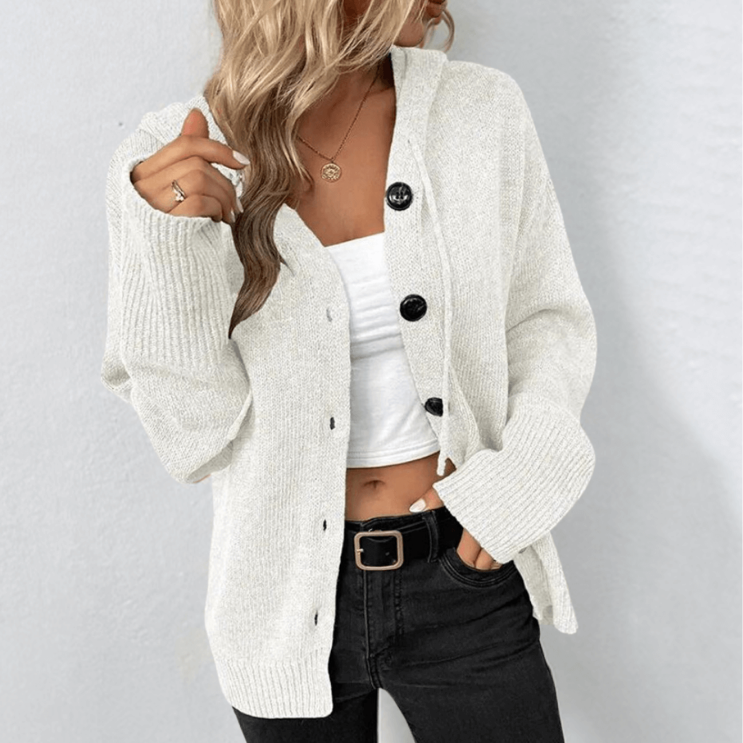 Femme portant un cardigan blanc en tricot avec boutons noirs, débardeur blanc et jean noir. Mode automne, style décontracté, tendance féminine.