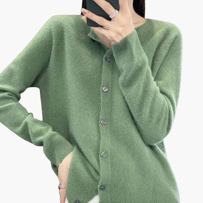 Femme portant un cardigan vert en cachemire, manches longues, avec boutons, tenant un smartphone. Mode automne-hiver, style élégant et confortable.