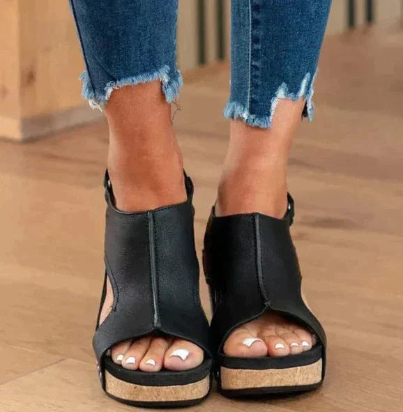 Sandales compensées noires en cuir, portées avec un jean déchiré. Chaussures d'été tendance pour femmes, confortables et élégantes.