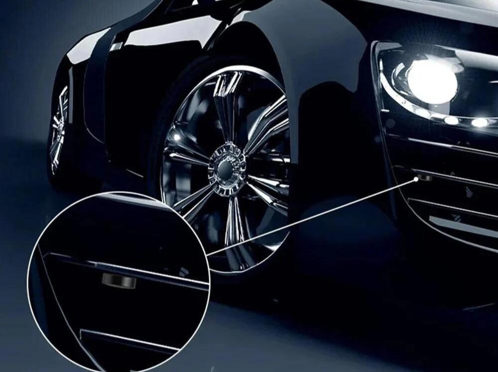 Voiture de luxe noire avec phares allumés, gros plan sur jantes chromées brillantes et détail de la caméra de recul. Design moderne et élégant.