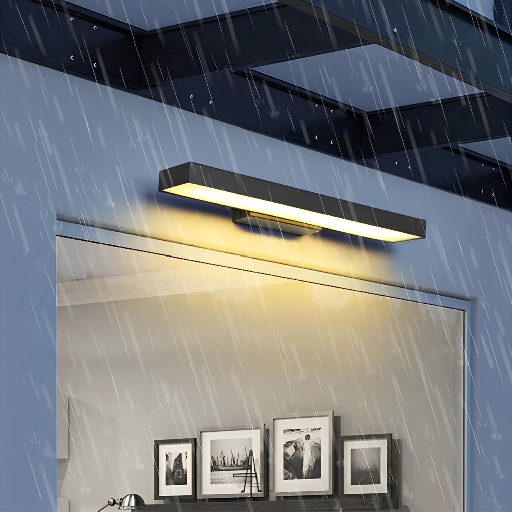 Applique murale extérieure moderne éclairée sous la pluie, fixée sur une façade en verre, illuminant des cadres photo en noir et blanc à l'intérieur.