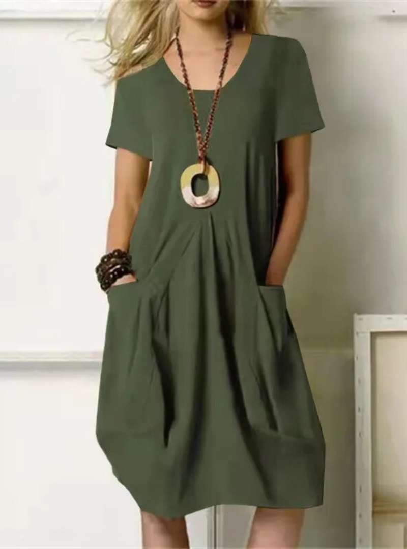 Robe verte ample avec poches, collier pendentif rond, femme blonde. Mode décontractée, style estival, tenue élégante et confortable.