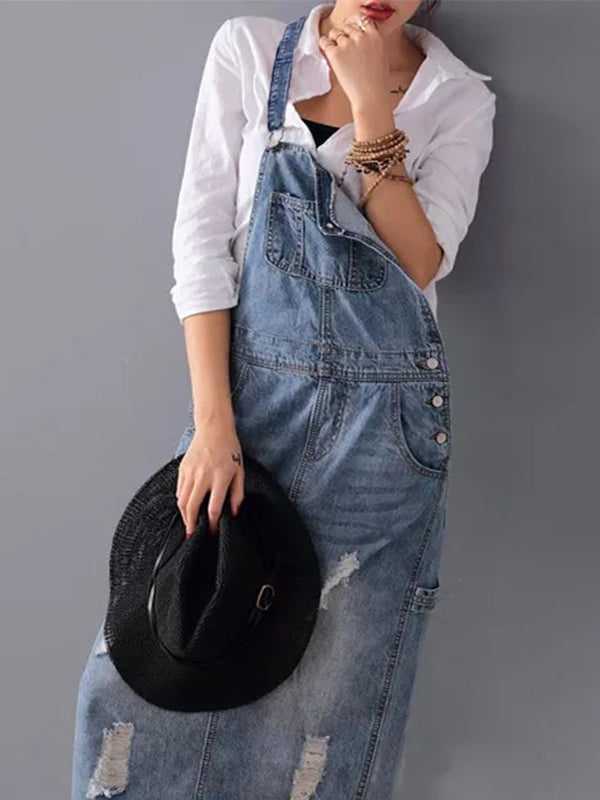 Femme en salopette en jean déchiré, chemise blanche, tenant un chapeau noir. Mode décontractée, tendance denim, style urbain chic.