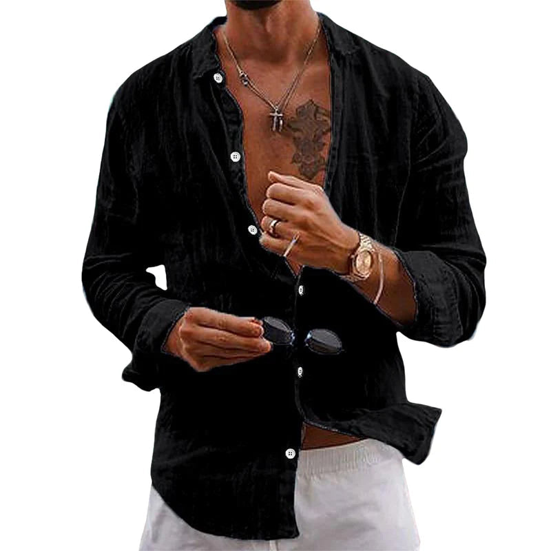 Homme portant une chemise noire ouverte, montrant un tatouage et un collier, tenant des lunettes de soleil, style décontracté et élégant.