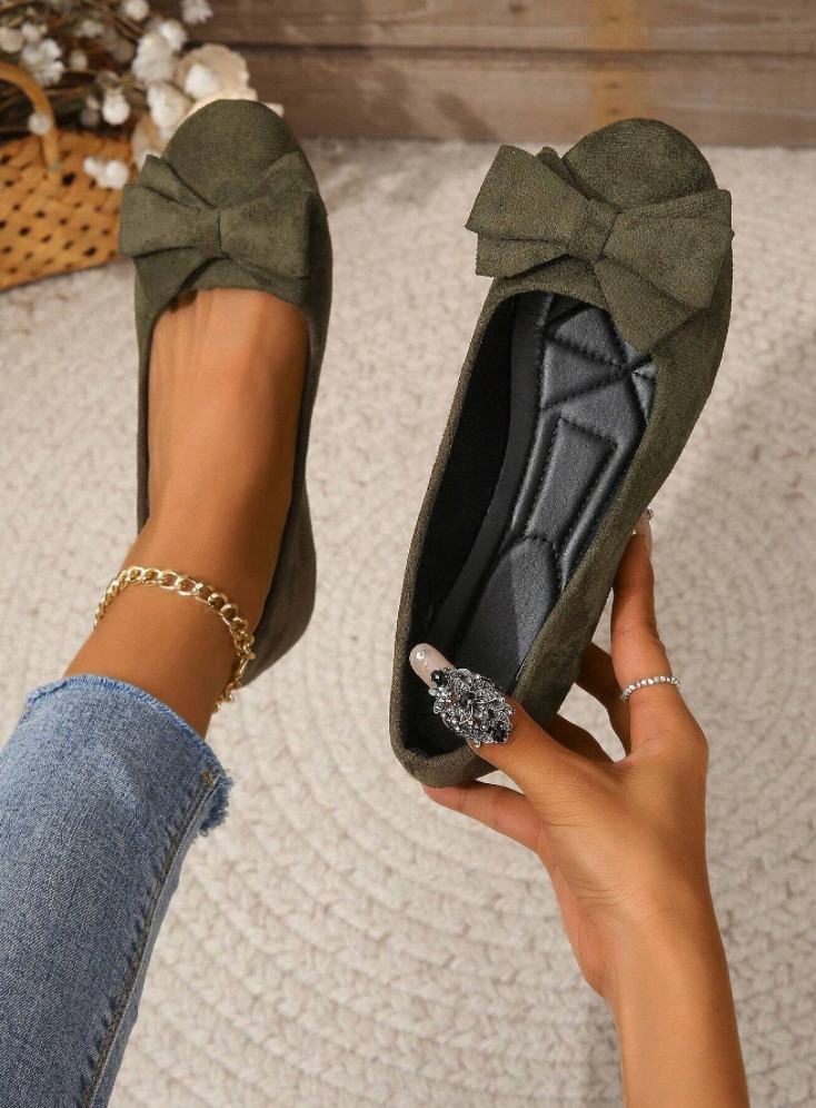 Ballerines vertes en daim avec nœud, portées par une personne en jean, sur fond de tapis beige. Chaussures élégantes et confortables pour femme.