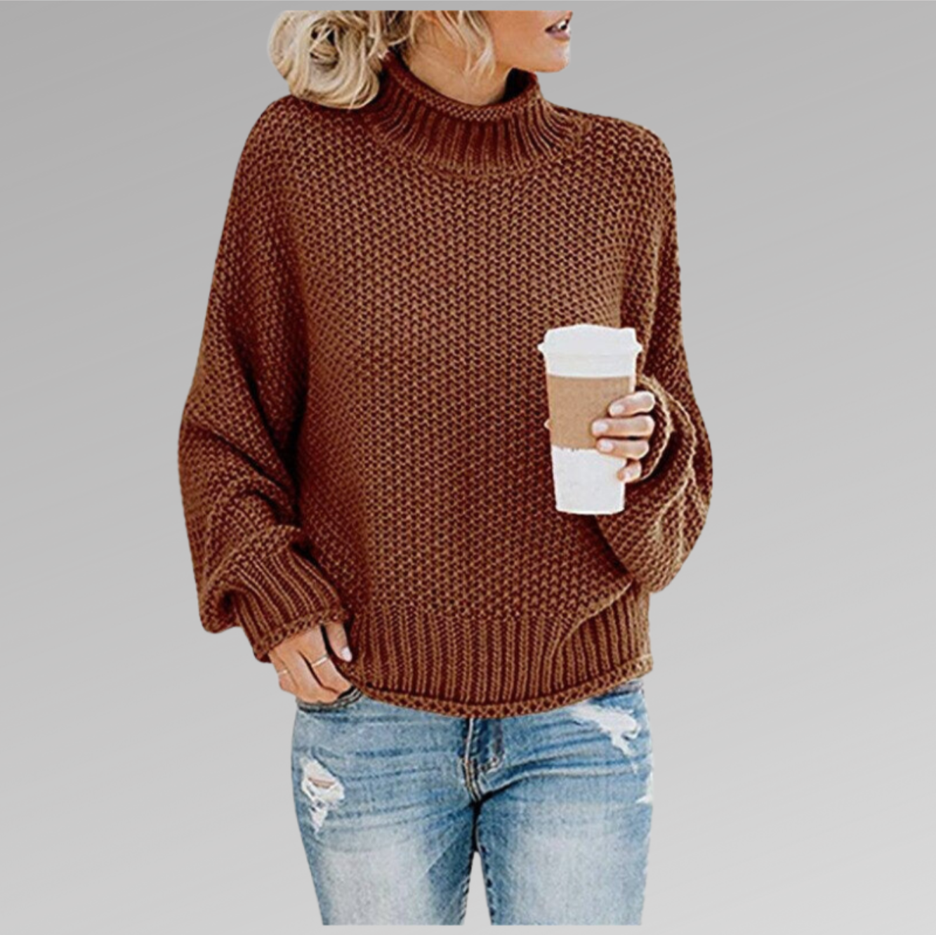 Femme portant un pull en maille marron avec un col roulé, tenant un gobelet de café, vêtue d'un jean déchiré. Mode automne-hiver décontractée.