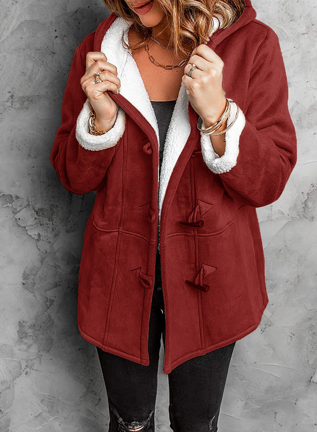 Femme portant un manteau rouge en laine avec doublure en fausse fourrure blanche, sur fond de mur gris. Mode hiver, style élégant et confortable.
