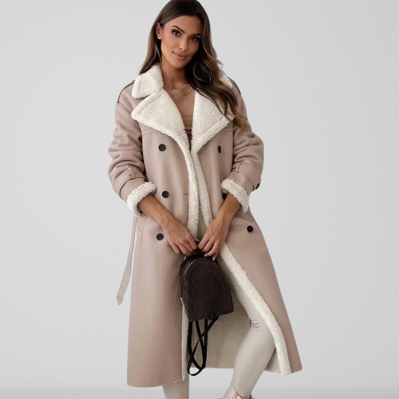 Femme portant un manteau long beige à doublure en fausse fourrure, tenant un sac à main noir. Mode hiver élégante, tendance vêtements chauds.