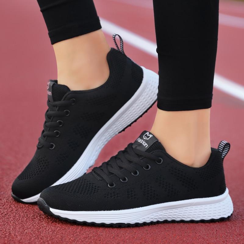 Chaussures de sport noires pour femme sur piste de course rouge, semelle blanche, design respirant, idéales pour la course et le fitness.