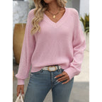 Femme portant un pull rose en maille ajourée avec un col en V, associé à un jean bleu et une ceinture blanche. Mode féminine décontractée.