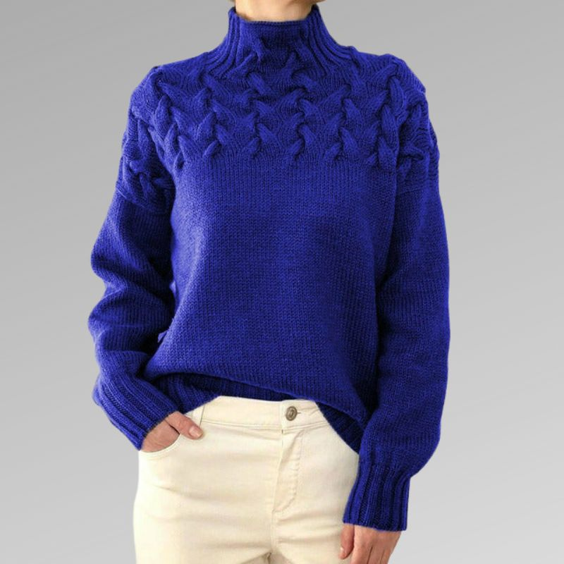 Pull bleu en laine torsadée pour femme, col montant, manches longues, porté avec un pantalon beige. Mode hiver élégante et confortable.