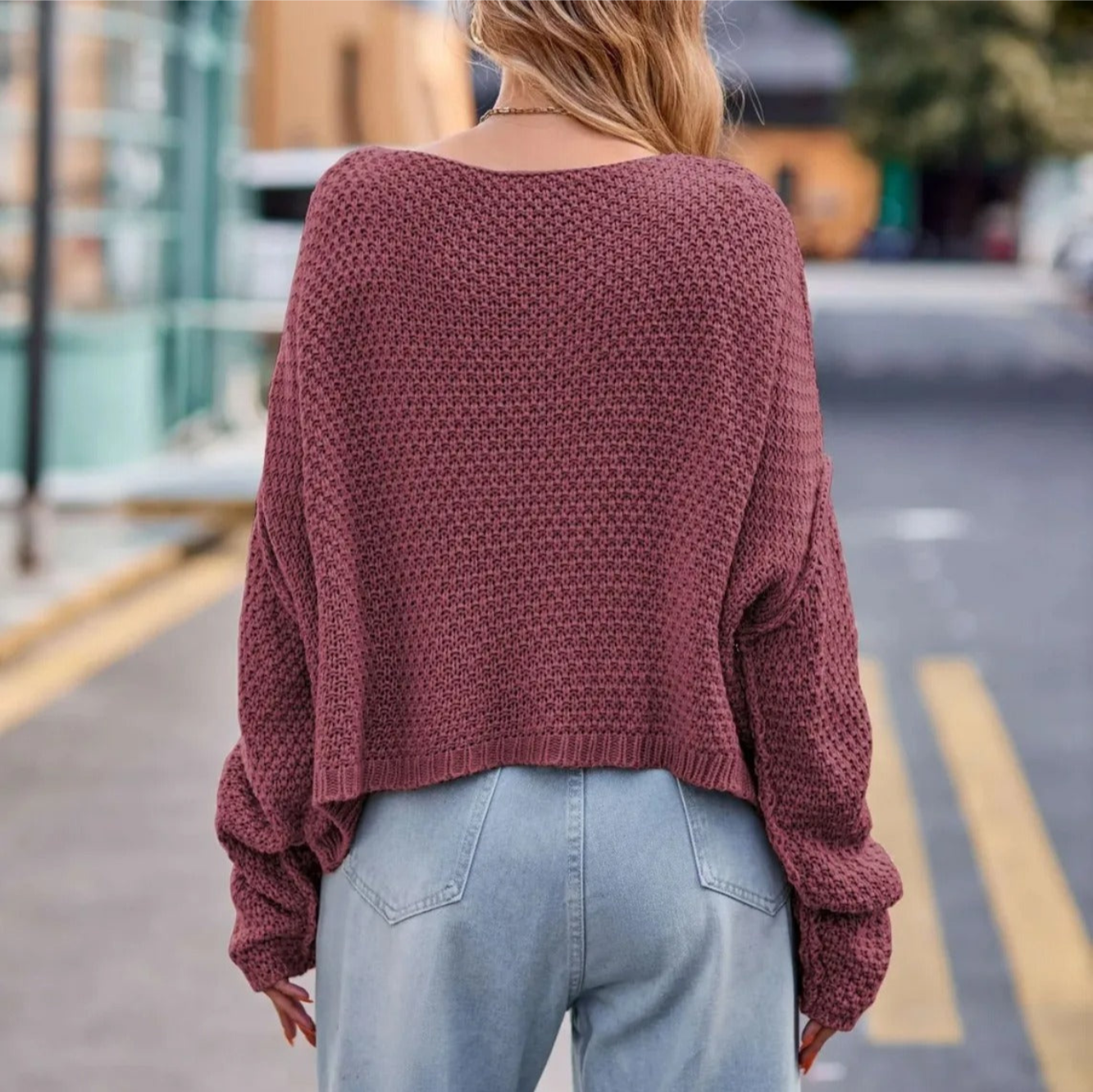 Femme portant un pull en tricot rose ample et un jean bleu clair, marchant en ville. Mode automne, style décontracté, tendance urbaine.