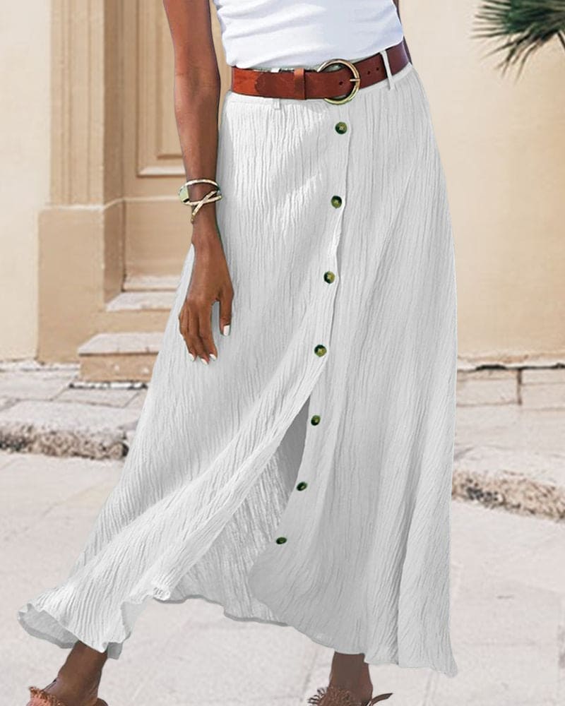 Femme portant une jupe longue blanche boutonnée, ceinture marron, top blanc. Mode estivale élégante, tenue décontractée chic, style urbain.