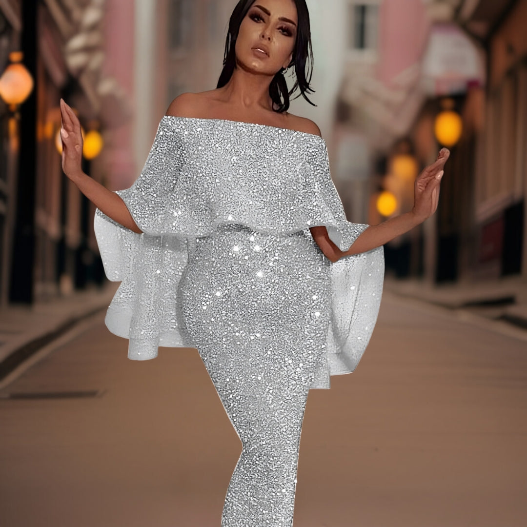 Robe de soirée argentée scintillante, manches évasées, portée par une femme élégante dans une rue urbaine illuminée. Mode glamour, tenue chic.