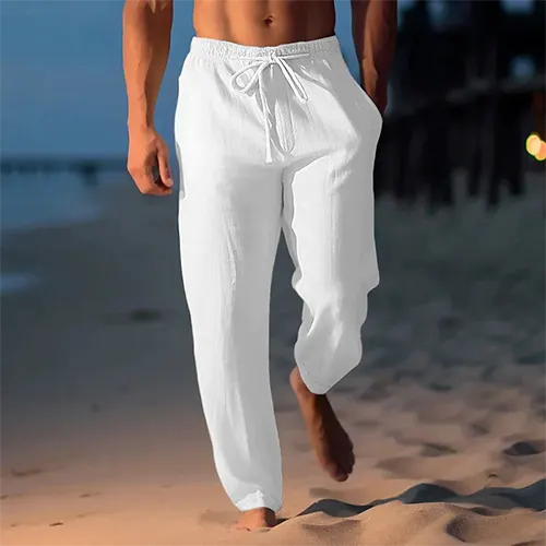 Homme marchant sur la plage au crépuscule, portant un pantalon blanc en lin. Mode estivale, détente bord de mer, vêtements légers pour homme.