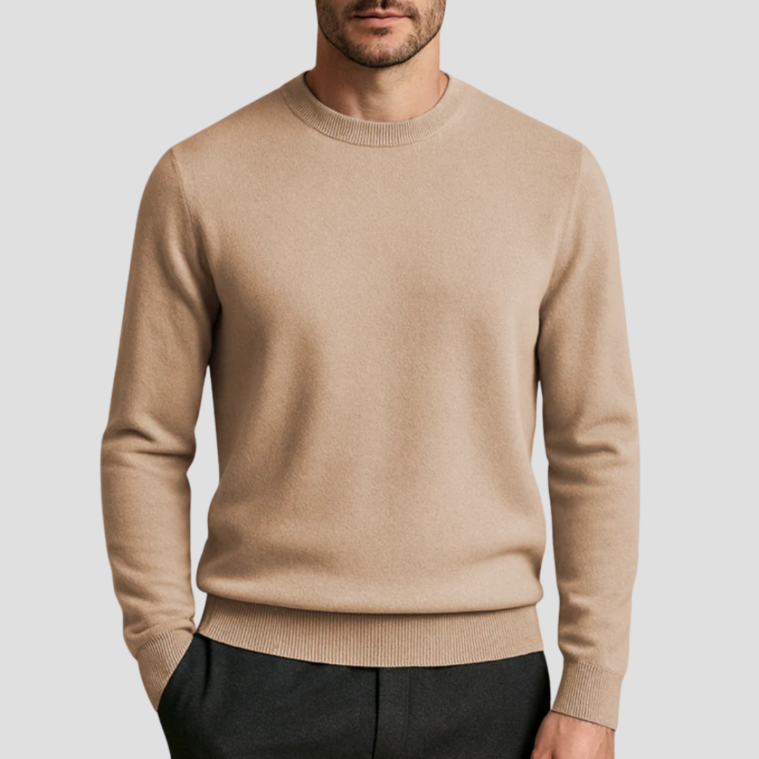 Homme portant un pull beige en laine, col rond, manches longues, avec pantalon noir. Mode masculine élégante et décontractée.