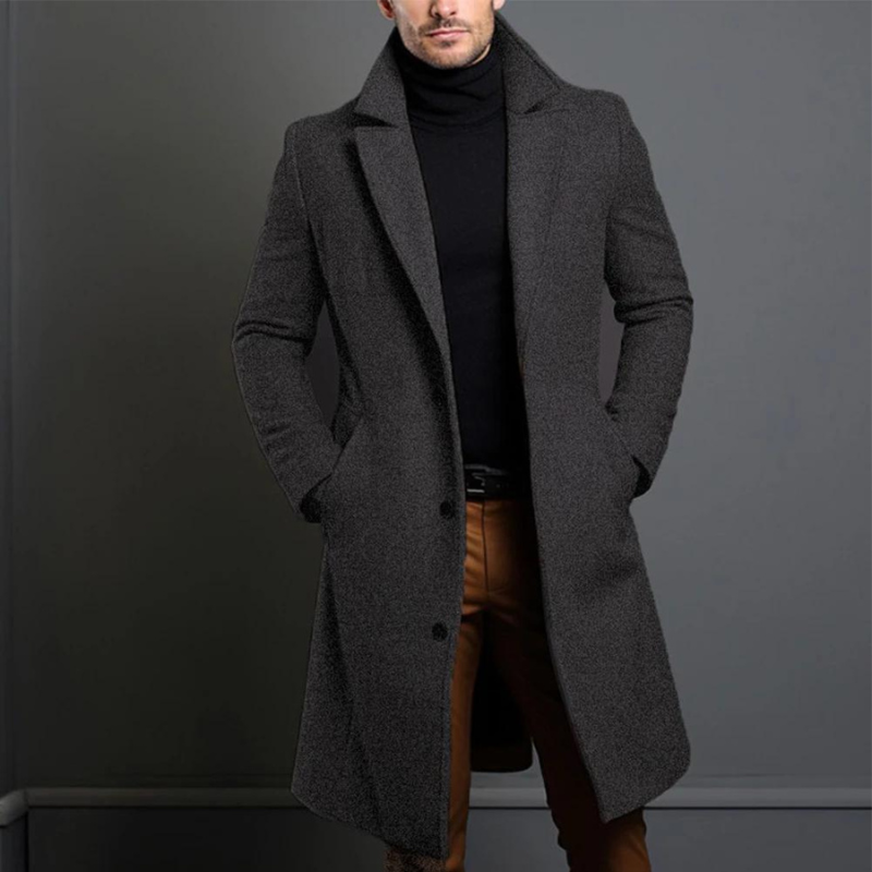 Homme portant un manteau gris élégant, col relevé, sur un pull noir et un pantalon marron. Mode masculine, style automne-hiver, tenue chic.