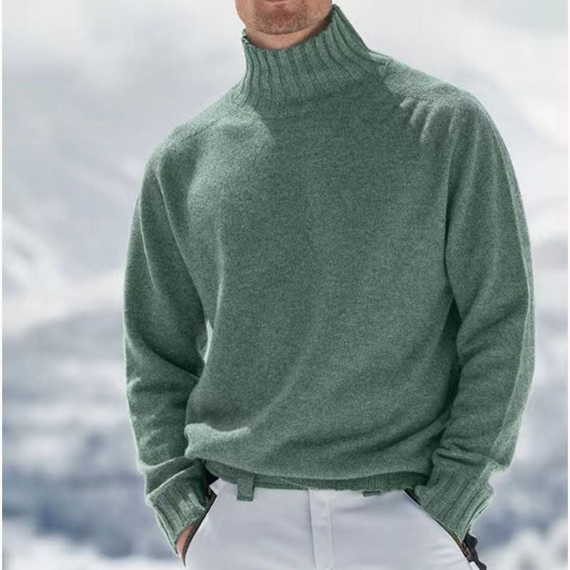 Homme portant un pull col roulé vert en laine, style hiver, devant un paysage enneigé. Mode masculine, vêtements chauds, tendance hiver.