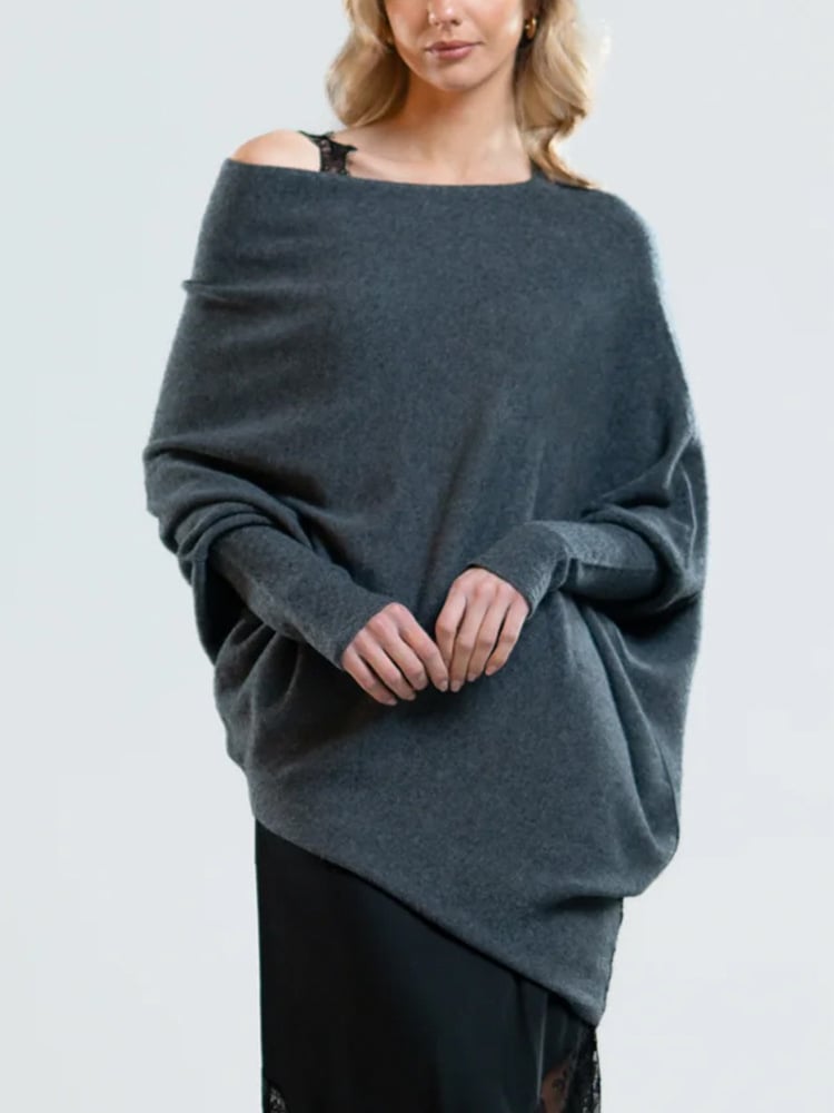 Femme portant un pull oversize gris en cachemire, style décontracté, avec une épaule dénudée. Mode automne-hiver, élégance et confort.