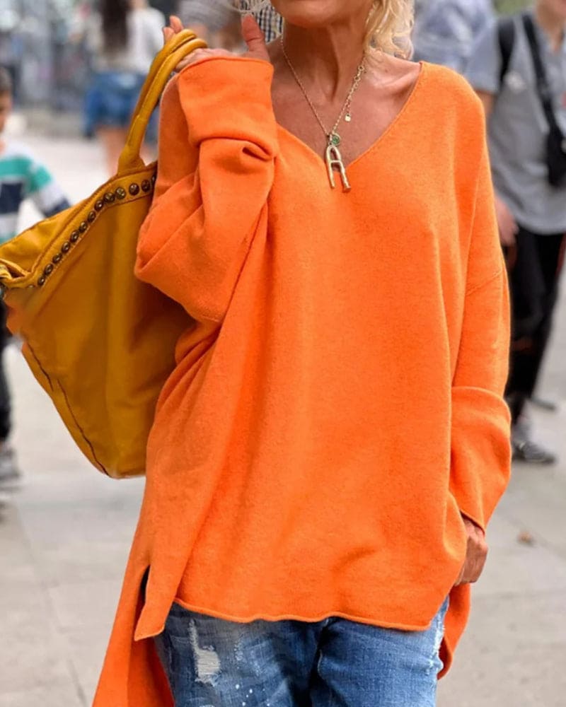 Femme portant un pull orange vif, sac à main jaune, collier doré, et jeans décontractés. Mode automne, style urbain, tendance vêtements colorés.