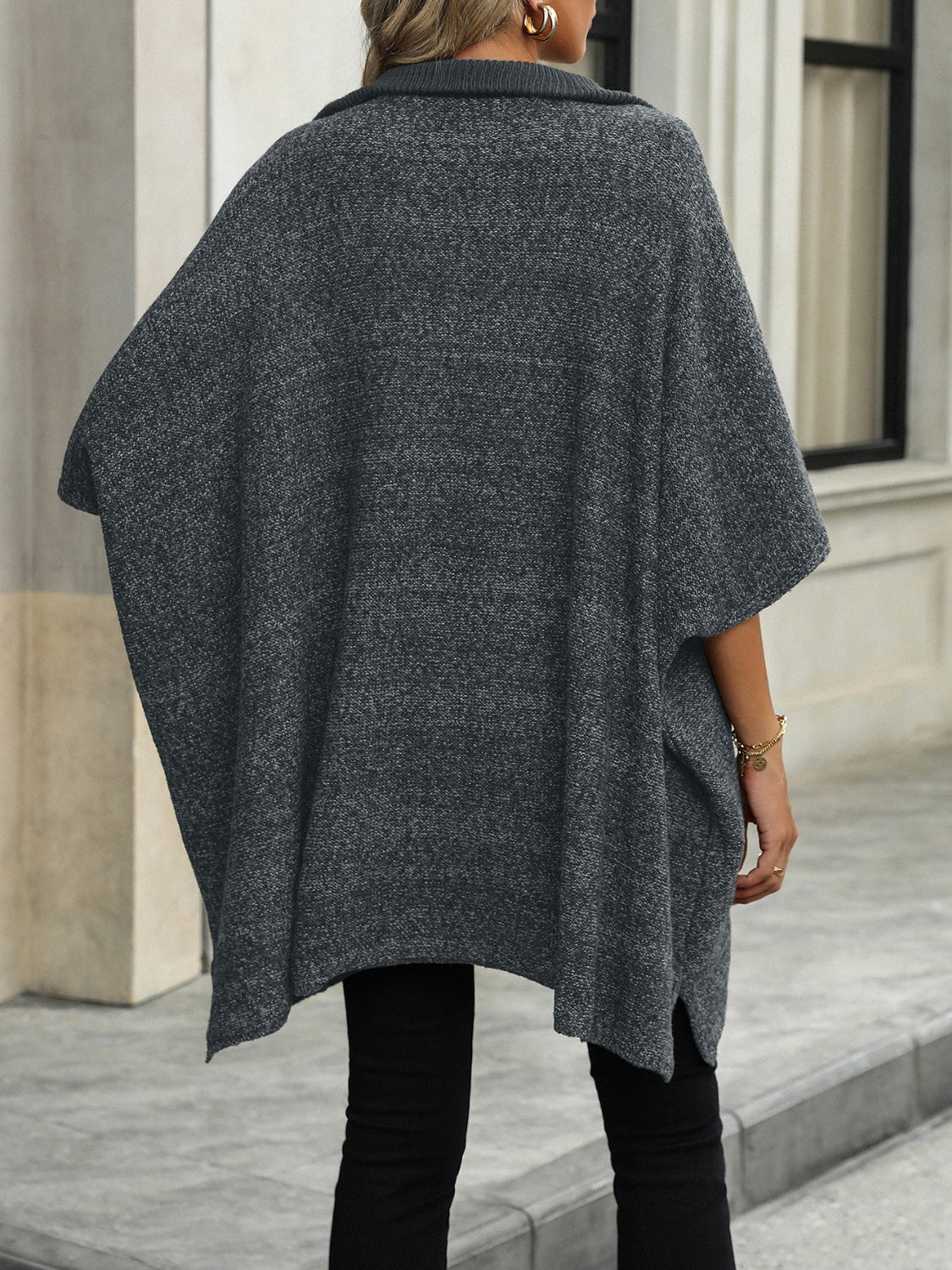 Femme portant un poncho gris en tricot, style décontracté, devant un bâtiment moderne. Mode automne-hiver, tenue élégante et confortable.