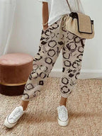 Femme portant un pantalon beige à motifs noirs, t-shirt blanc, baskets blanches et sac en osier. Mode décontractée, tendance et élégante.