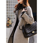 Femme portant un manteau gris élégant avec sac à main noir matelassé à chaîne dorée, mode automne chic, style urbain sophistiqué.