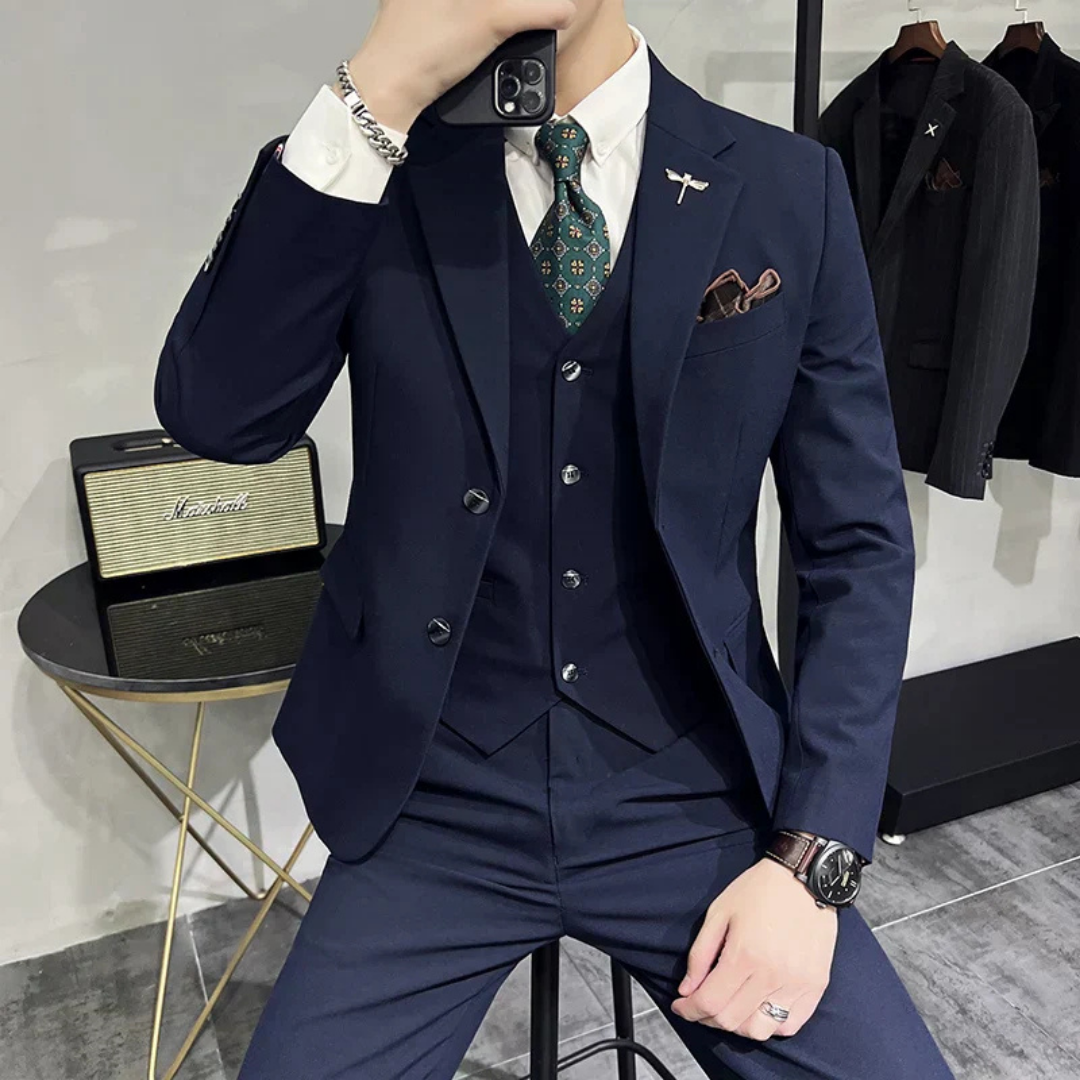 Homme en costume bleu marine élégant, cravate à motifs, montre-bracelet, tenant un smartphone. Style formel, mode masculine, accessoires modernes.