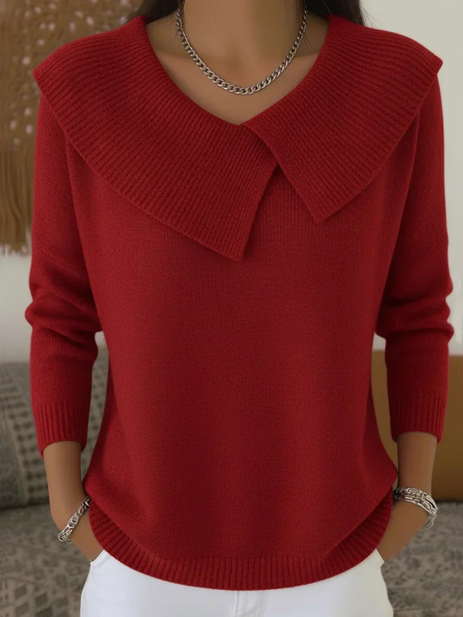 Femme portant un pull rouge élégant avec col large, manches longues, chaîne argentée, posant devant un fond neutre. Mode automne-hiver chic.