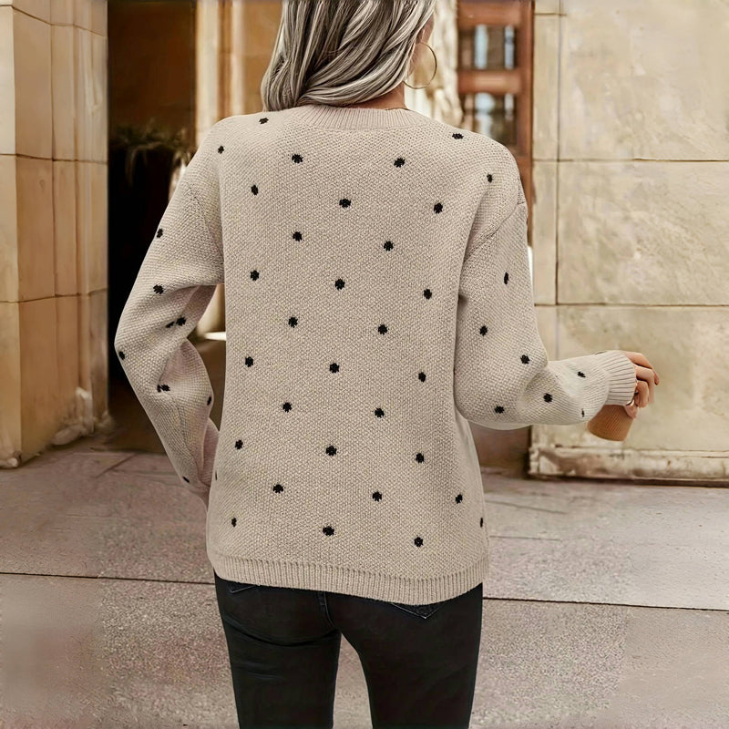 Femme portant un pull beige à pois noirs, vue de dos, dans un cadre urbain. Mode automne, style décontracté, tendance vêtements femme.