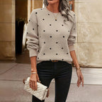Femme portant un pull beige à pois noirs, tenant un sac à main matelassé blanc. Mode automne, style décontracté chic, accessoires élégants.