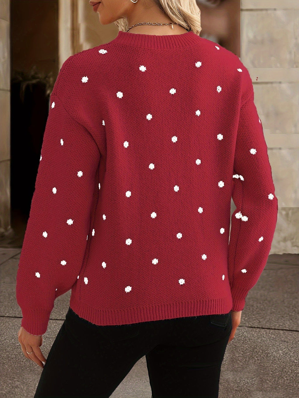 Femme portant un pull rouge à pois blancs, manches longues, col rond, style décontracté, mode automne-hiver, arrière-plan urbain flou.