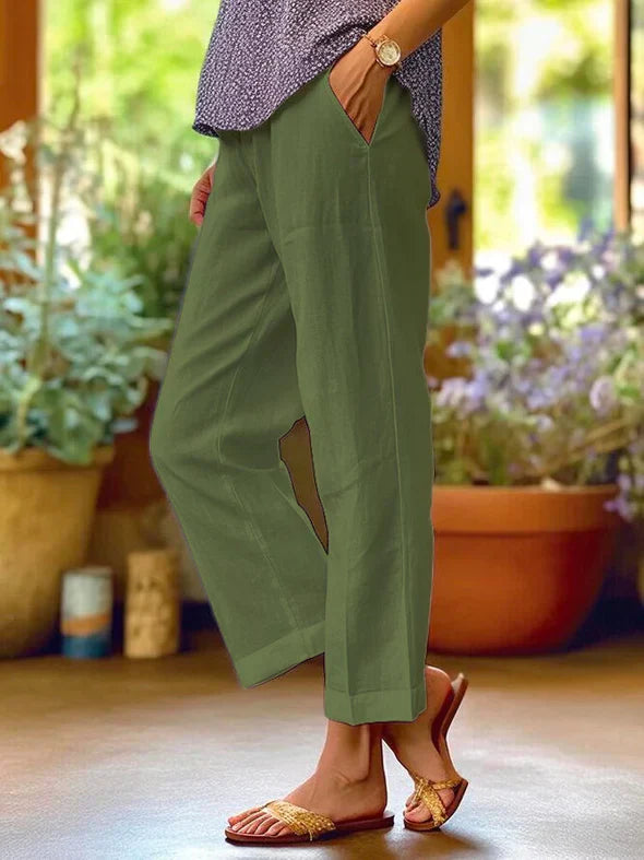 Pantalon vert kaki femme, coupe ample, poches latérales, porté avec sandales dorées et chemisier à motifs, ambiance jardin en arrière-plan.