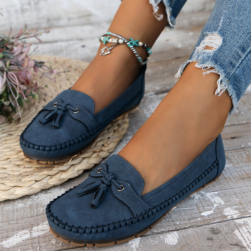 Chaussures mocassins bleu marine pour femme, avec nœuds décoratifs, portées avec un jean déchiré. Style décontracté et tendance.