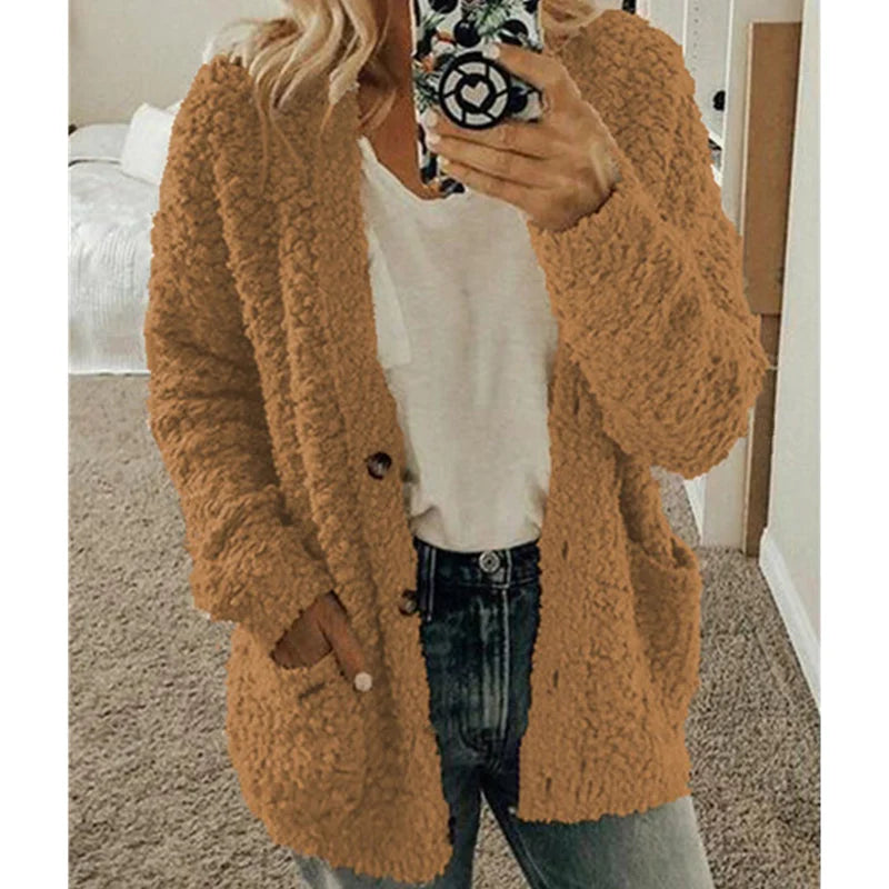 Femme portant un cardigan en laine beige, tenant un smartphone, vêtue d'un t-shirt blanc et d'un jean, dans une chambre moderne.