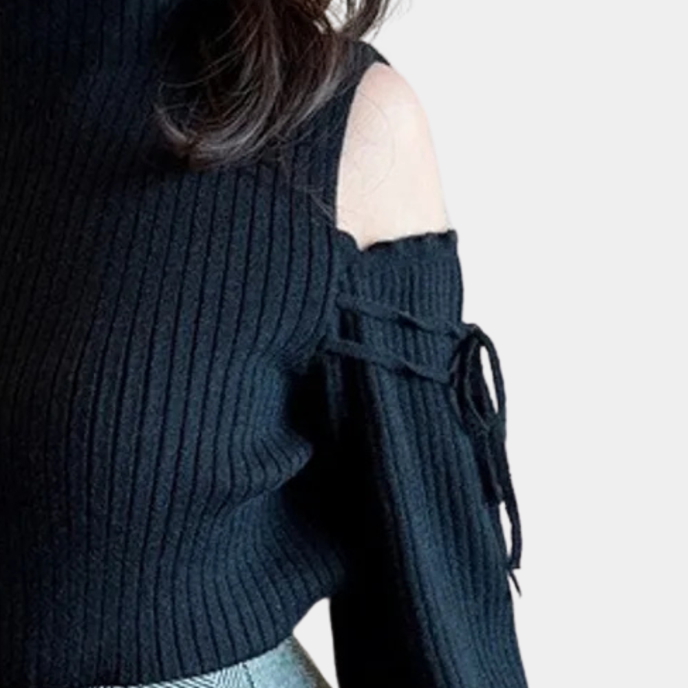 Femme portant un pull noir à épaules dénudées, manches longues avec lacets, associé à une jupe grise. Mode automne-hiver élégante et tendance.