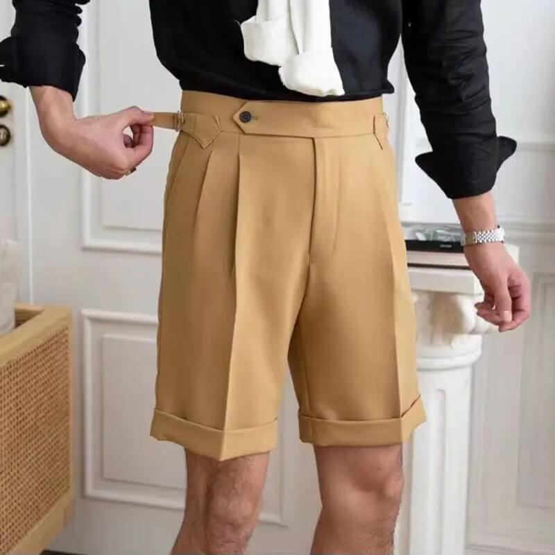 Homme ajustant un short beige élégant, chemise noire, intérieur moderne. Mode masculine, tenue décontractée chic, ajustement parfait.