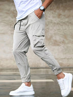 Homme portant un pantalon cargo beige avec poches latérales, t-shirt blanc et baskets blanches. Mode décontractée, style urbain, tendance masculine.